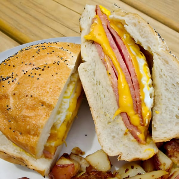 A sliced deli sandwich with ham, melted cheese, and egg, served with home fries.