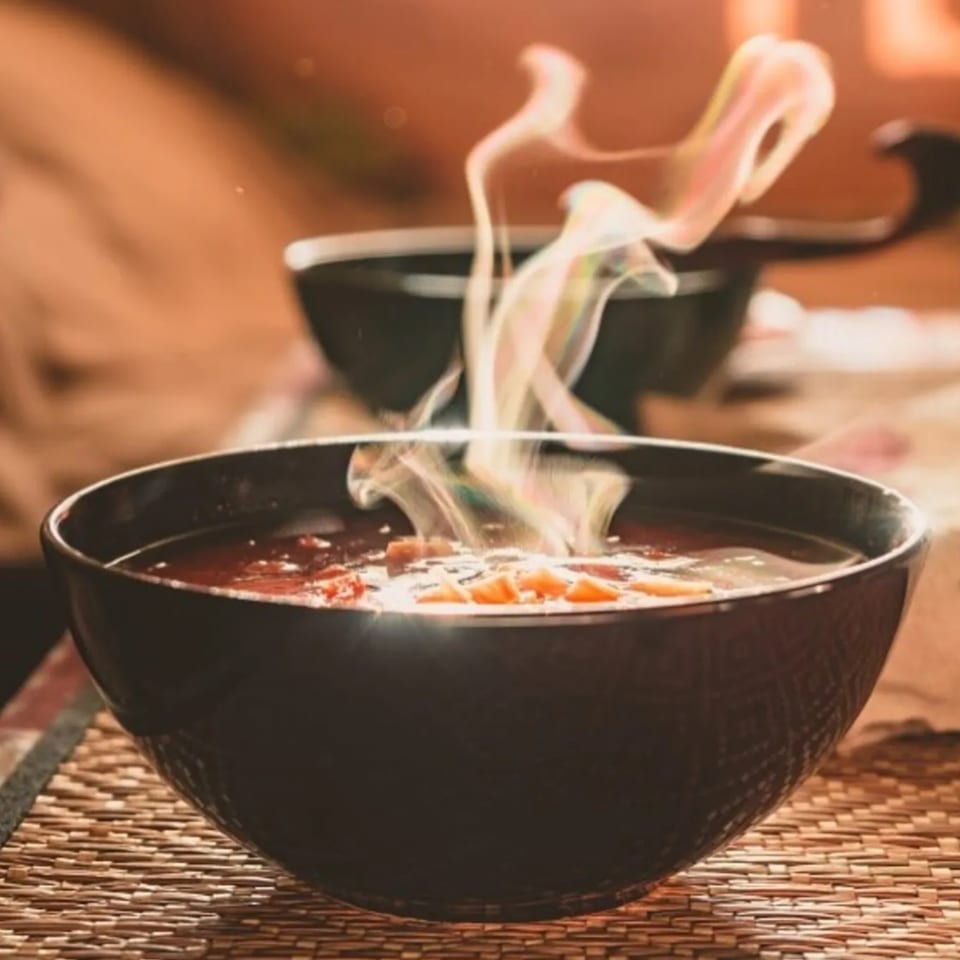 Steaming hot soup with vegetables in a black bowl on a woven placemat at Agamie Gourmet.