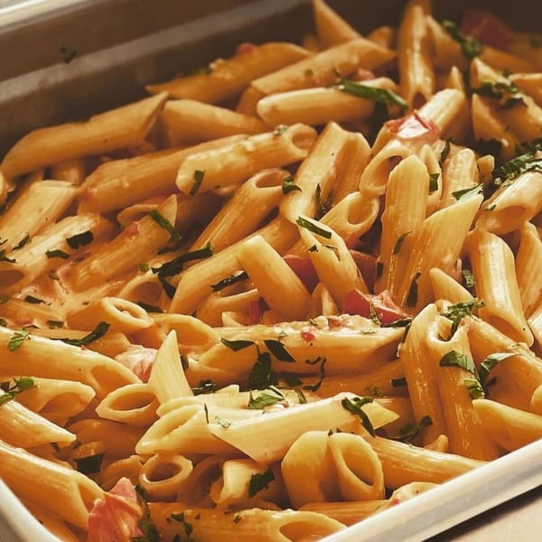 Creamy penne pasta with diced tomatoes and fresh herbs in a catering tray.